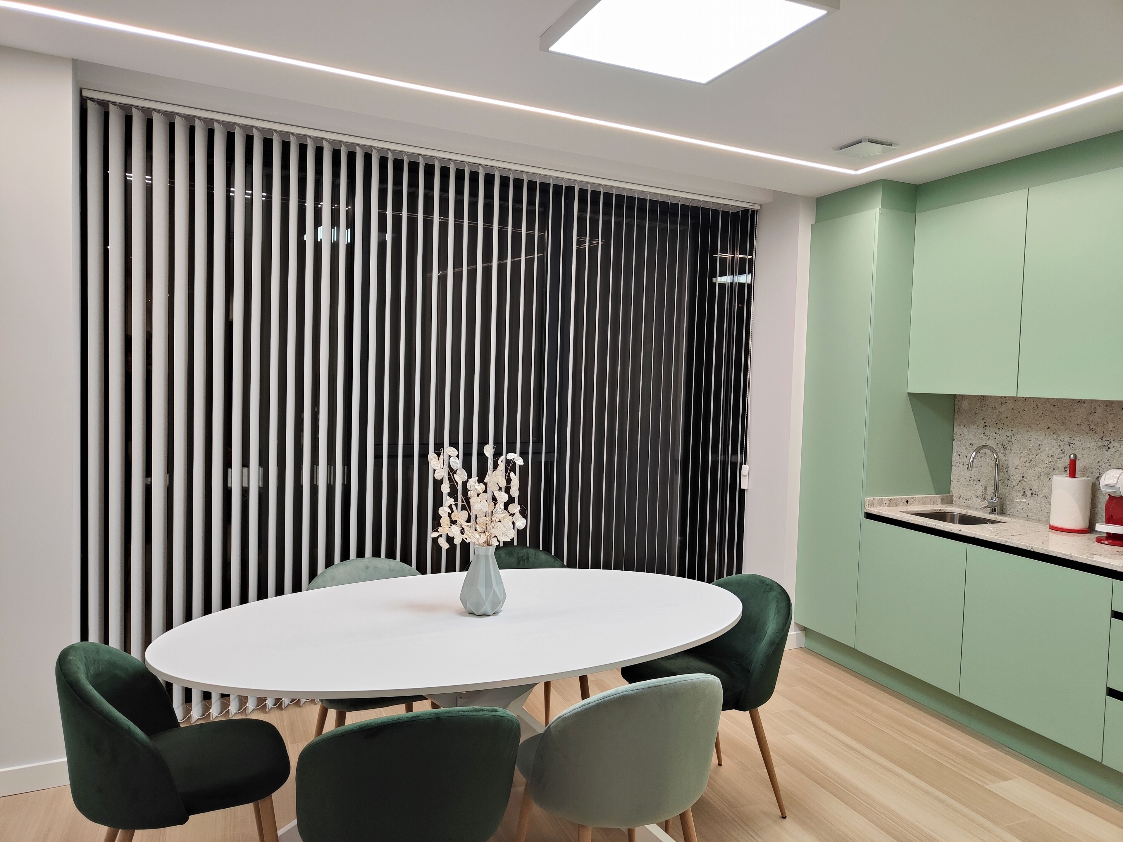 Een moderne keuken met groene kastjes, een wit aanrecht en een ronde eettafel met stoelen.