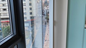 Ein Zimmer mit großem Fenster, Holzboden und Blick auf eine Stadt mit Gebäuden und einer Straße.