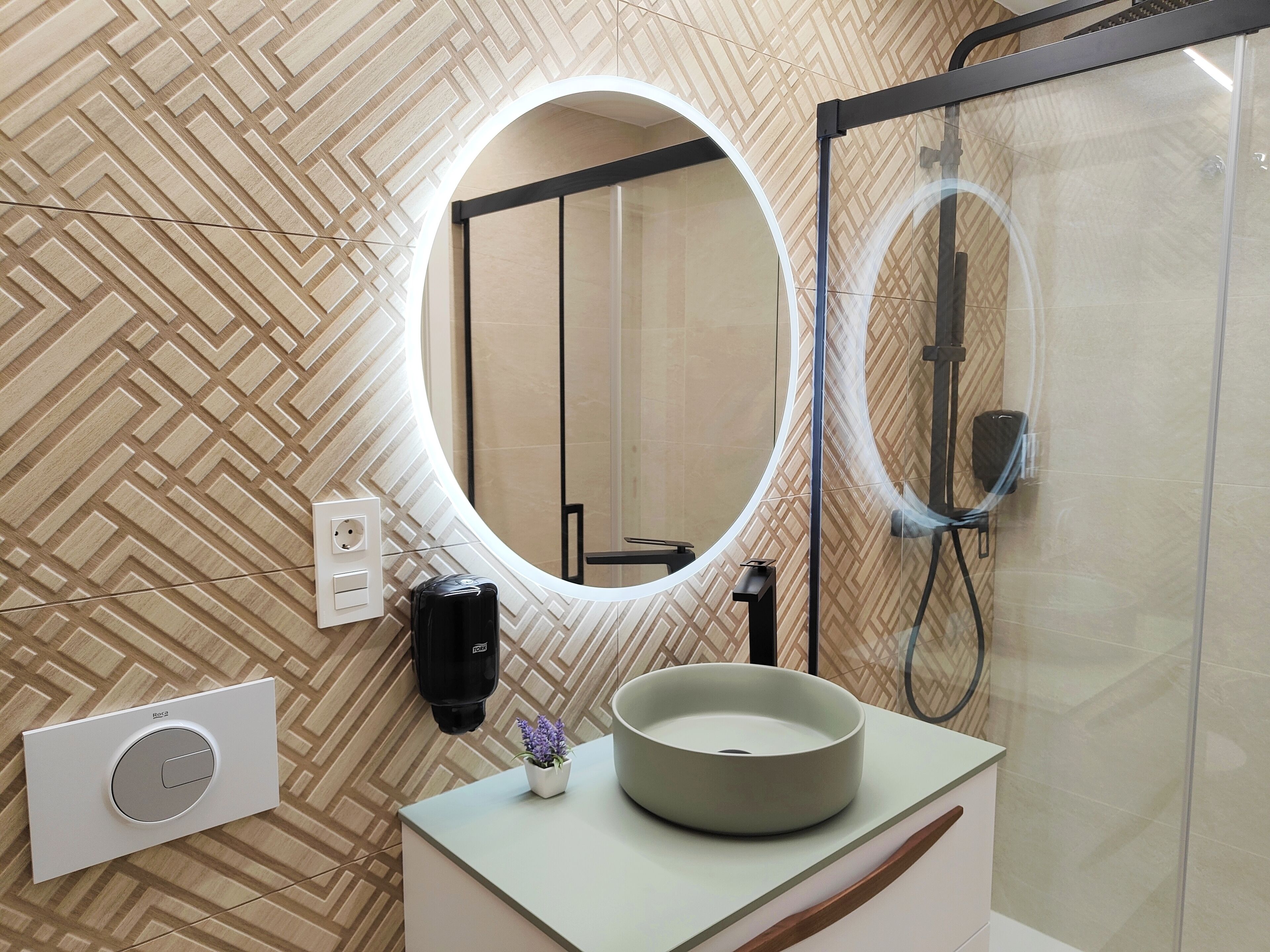 Un baño de diseño moderno, con un espejo redondo, un lavabo con forma de cuenco, una planta en maceta y una zona de ducha.