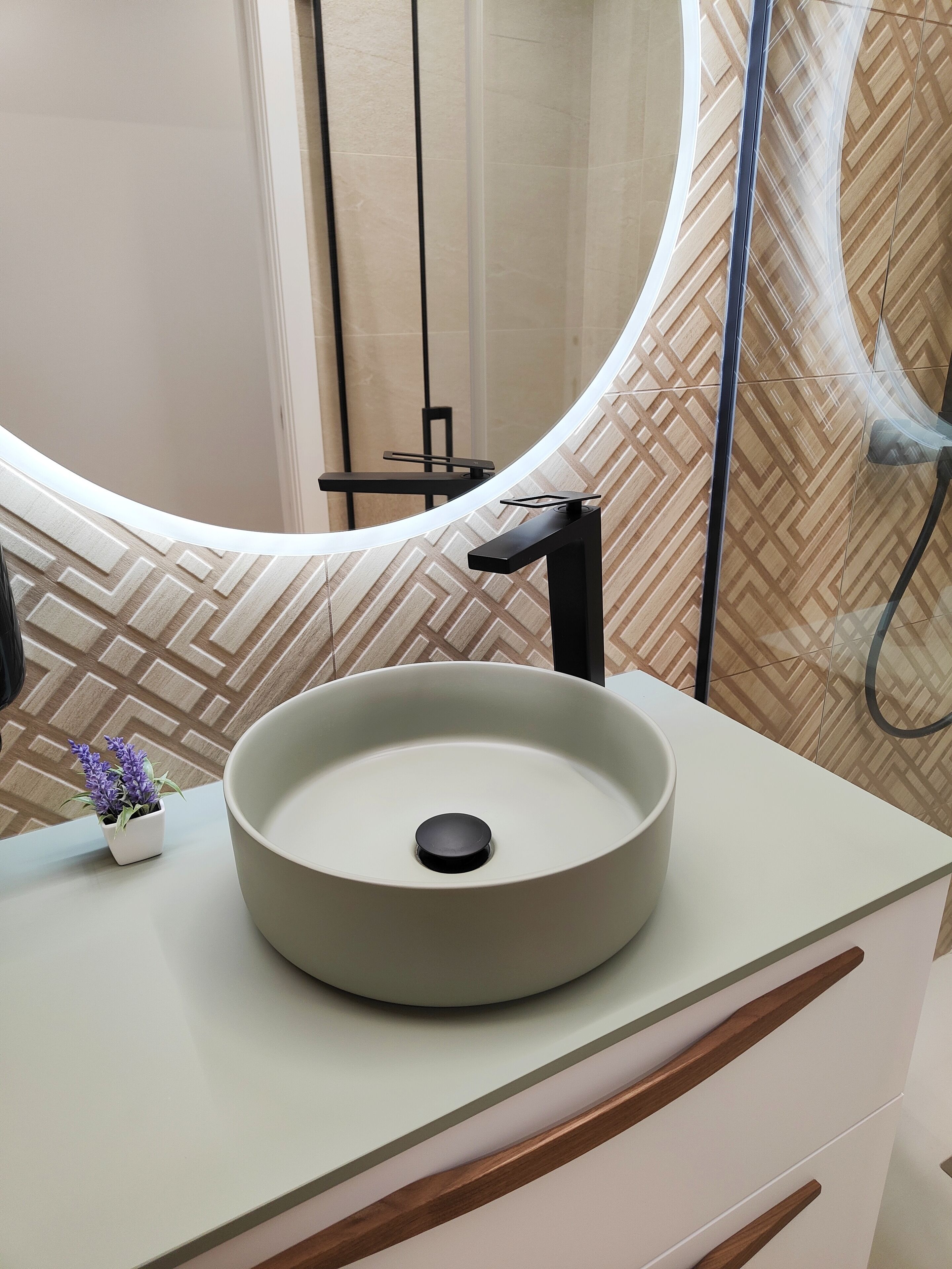 Een badkamer met een rond wastafel, een kleine plant in pot en een spiegel met een gebogen lijst.