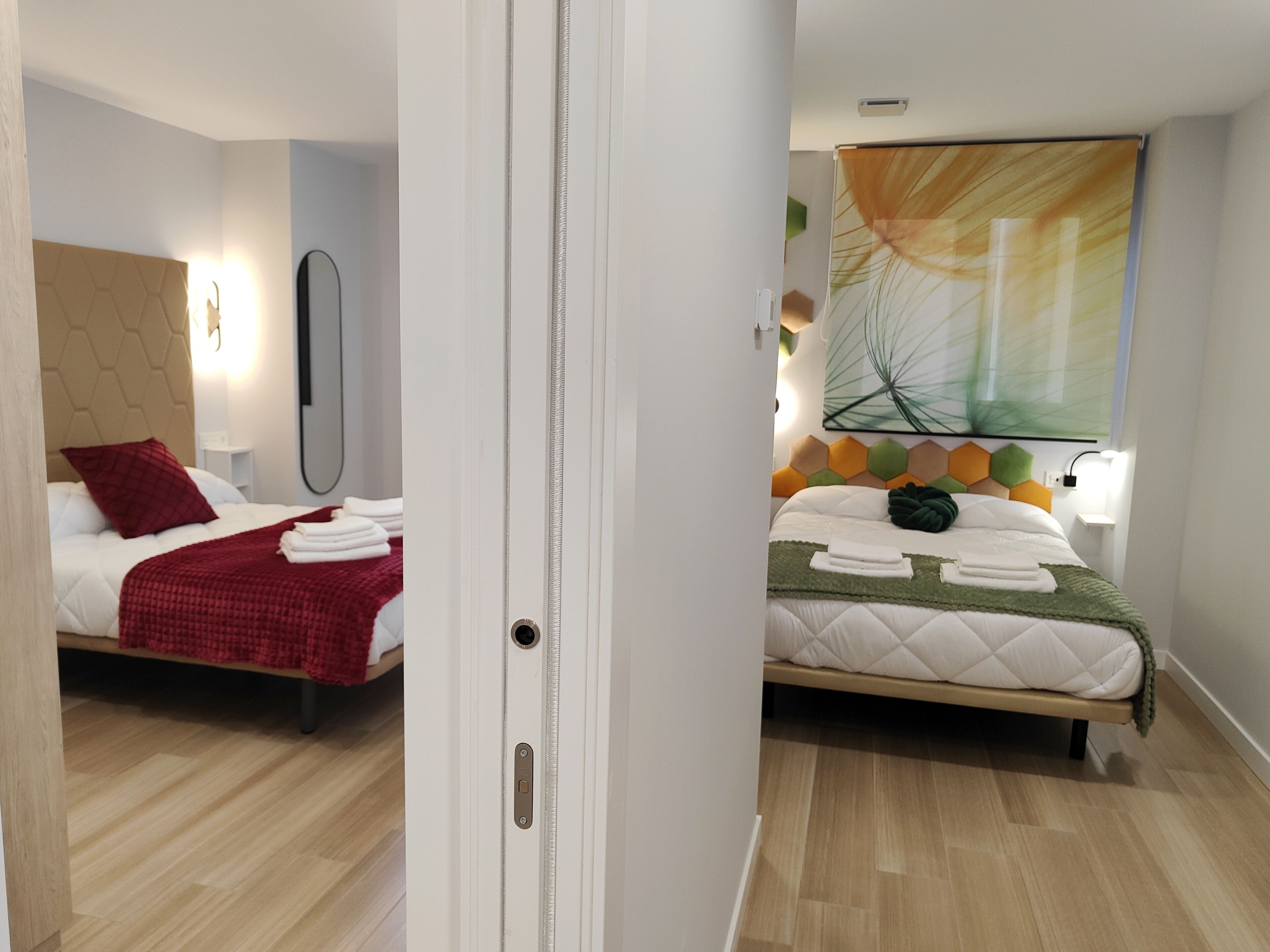 Una habitación de hotel con dos camas, cada una con un diseño de cabecera diferente, un ventanal con vistas y una puerta con manija.