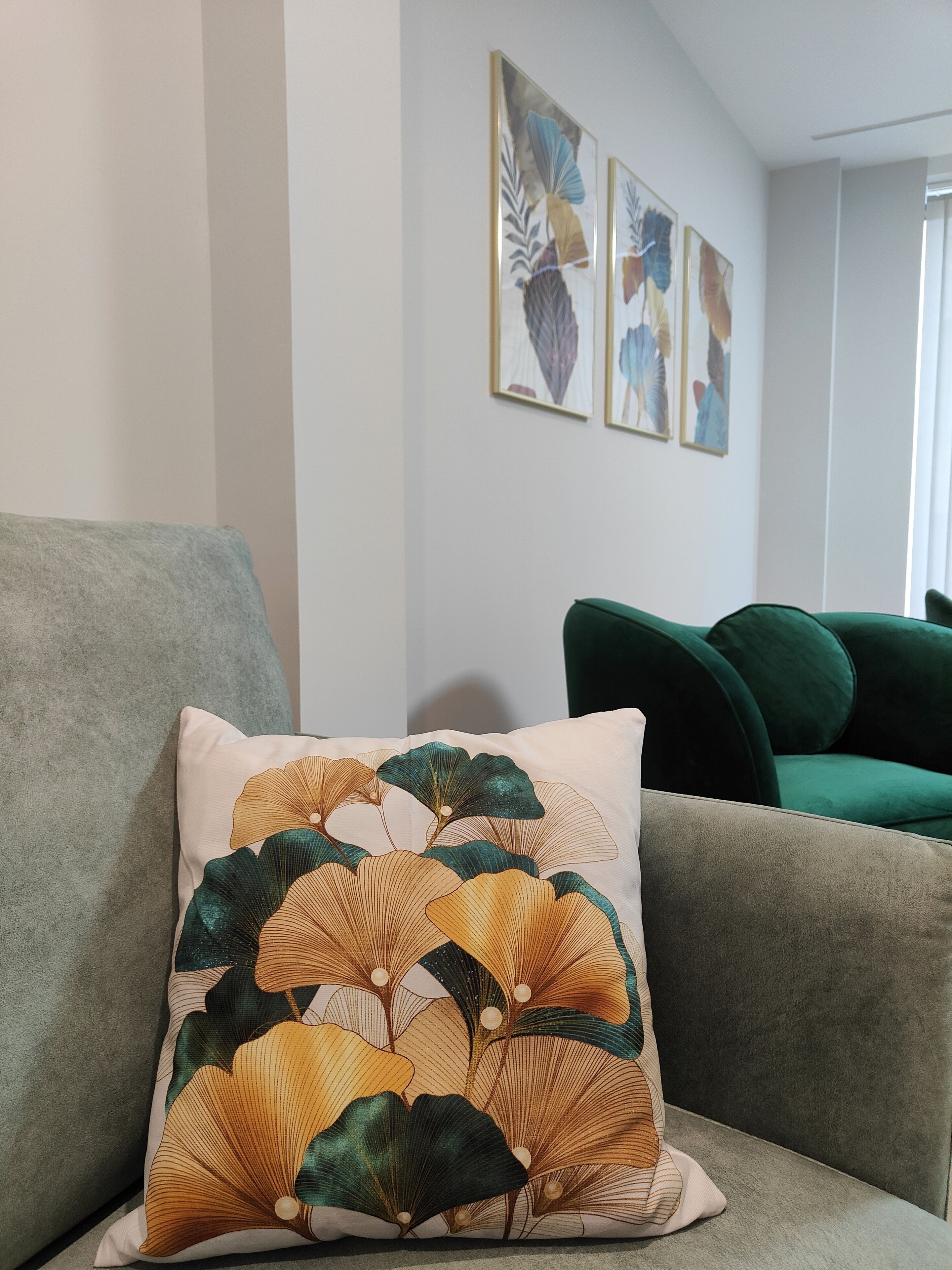 A living room with a grey sofa, a green sofa, and a decorative pillow with a leaf pattern.