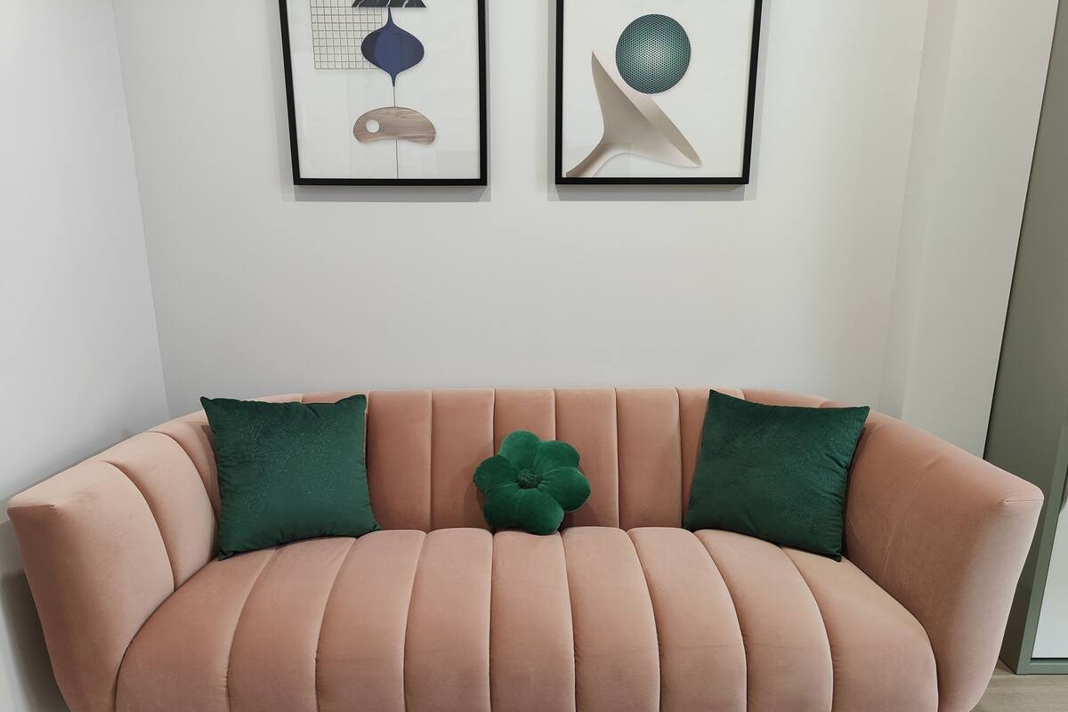 Un canapé rose agrémenté de coussins verts, deux œuvres d’art abstraites encadrées au-dessus, et un plancher en bois.