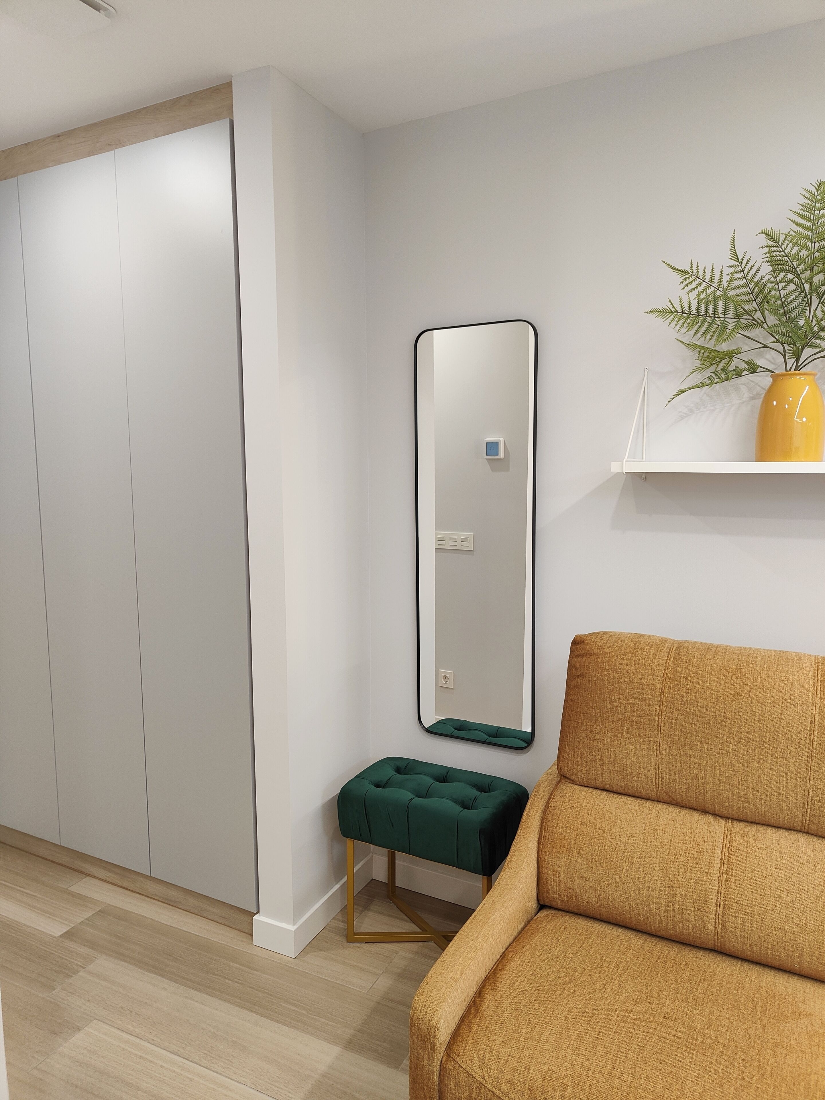 A modern room with a large wardrobe, a green ottoman, a yellow plant, and a mirror on the wall.