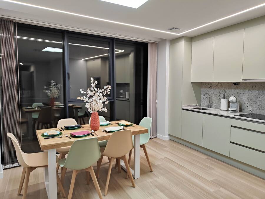 Un comedor moderno con una mesa de madera, sillas y un jarrón de flores blancas.