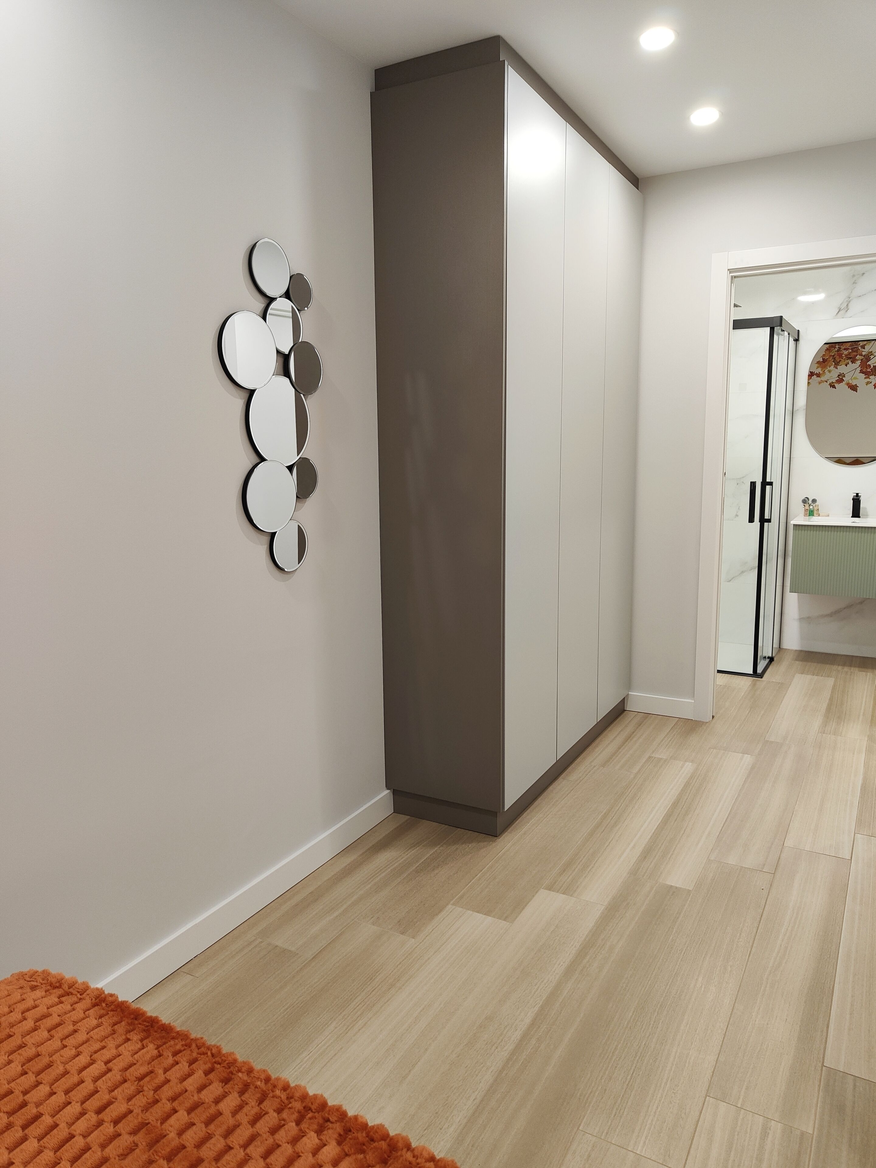 Een moderne hal met een garderobe, een decoratieve spiegelwand en een badkamer met een marmeren wastafel.