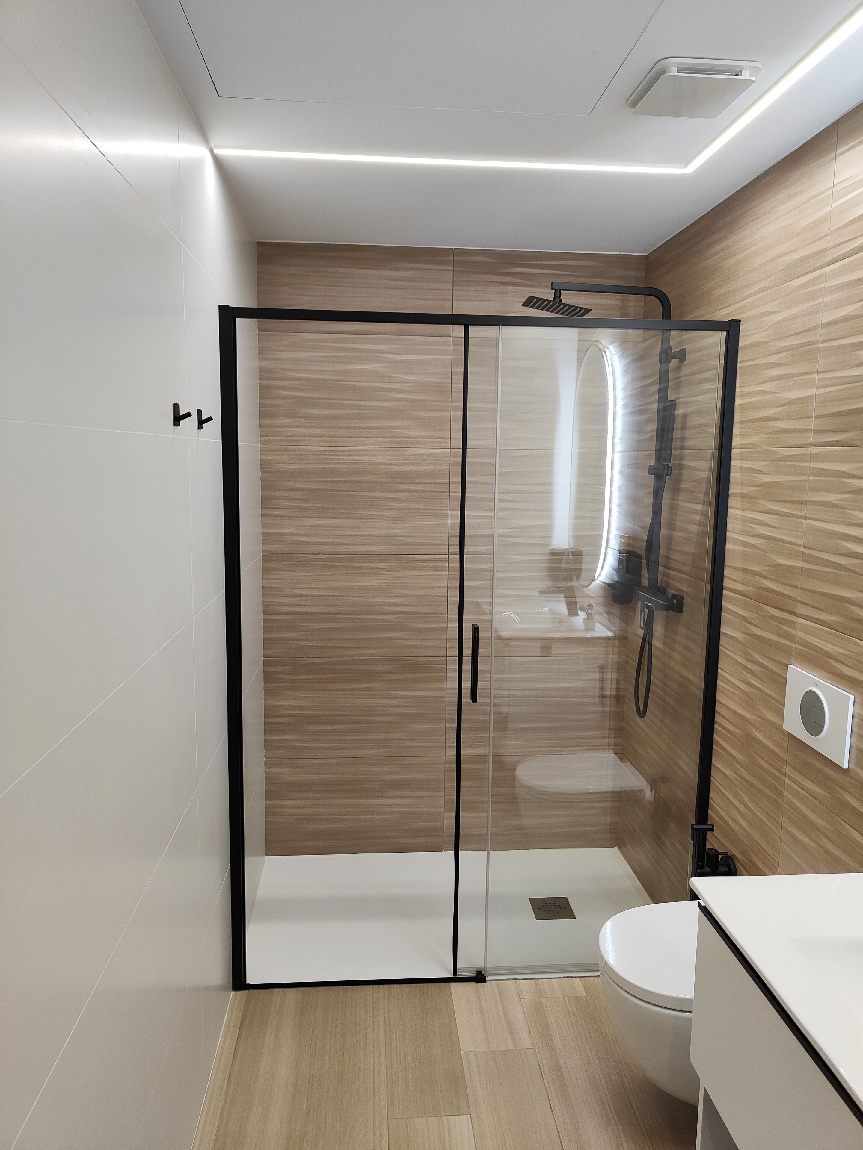A modern bathroom with a glass-enclosed shower, a white toilet, and a wooden vanity.