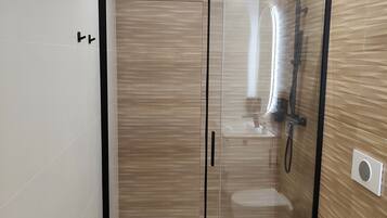 A modern bathroom with a glass-enclosed shower, a white toilet, and a wooden vanity.