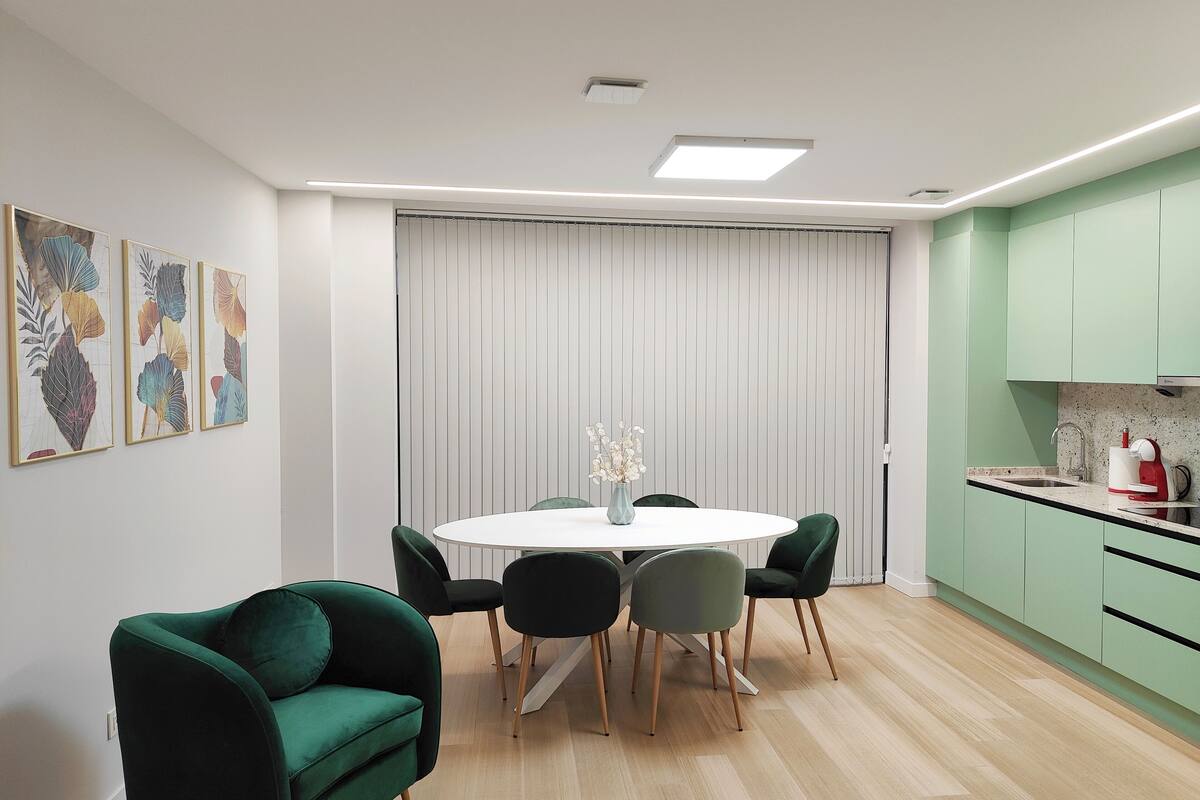 Une cuisine moderne avec des meubles de rangement verts, une table à manger blanche et un canapé vert.