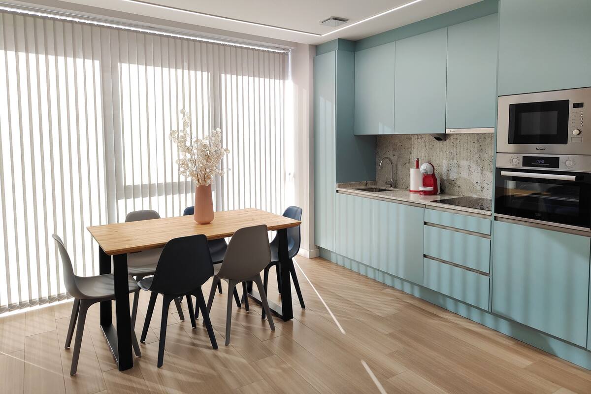 Une cuisine moderne avec des meubles de couleur bleu clair, une table à manger en bois et des chaises noires.