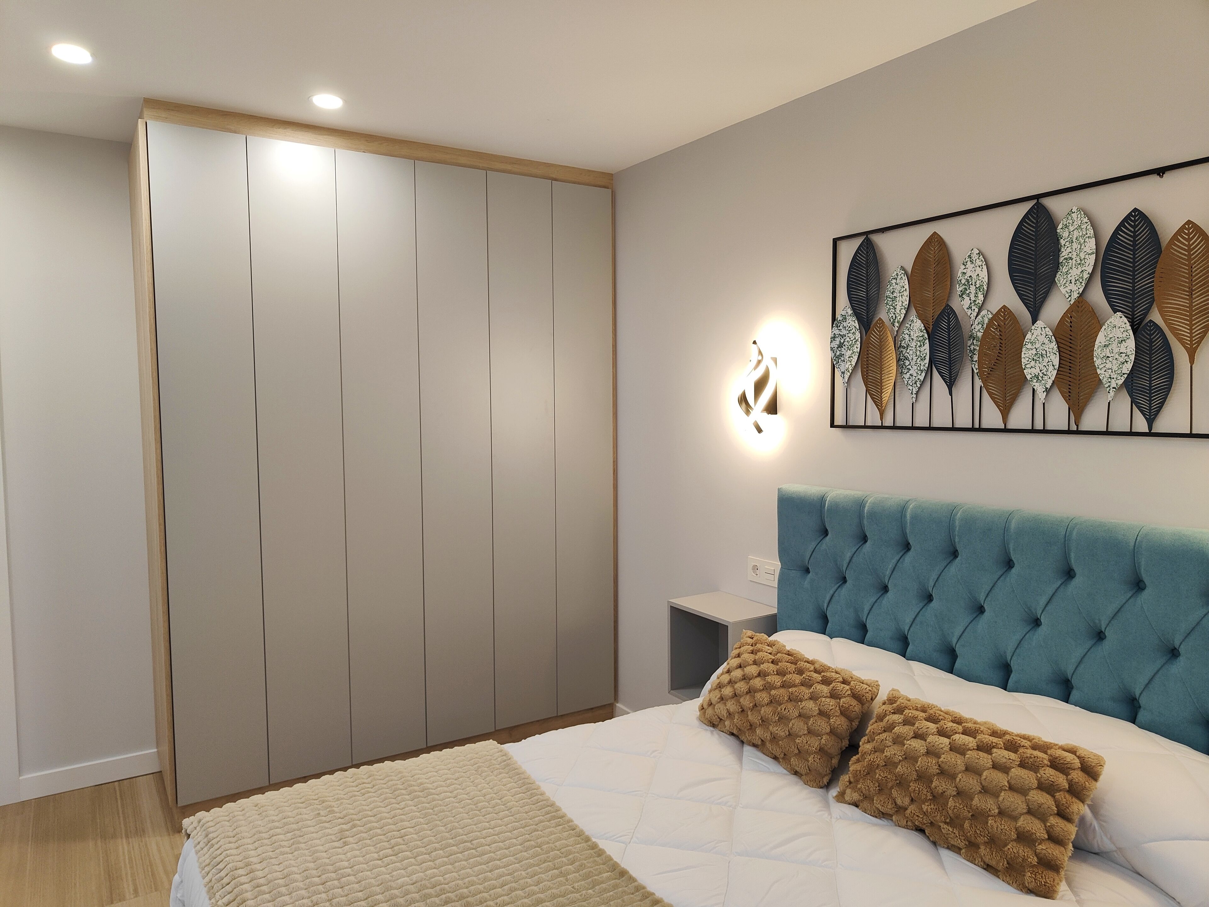 Un dormitorio con cama, armario, mesita de noche y lámpara de pared.