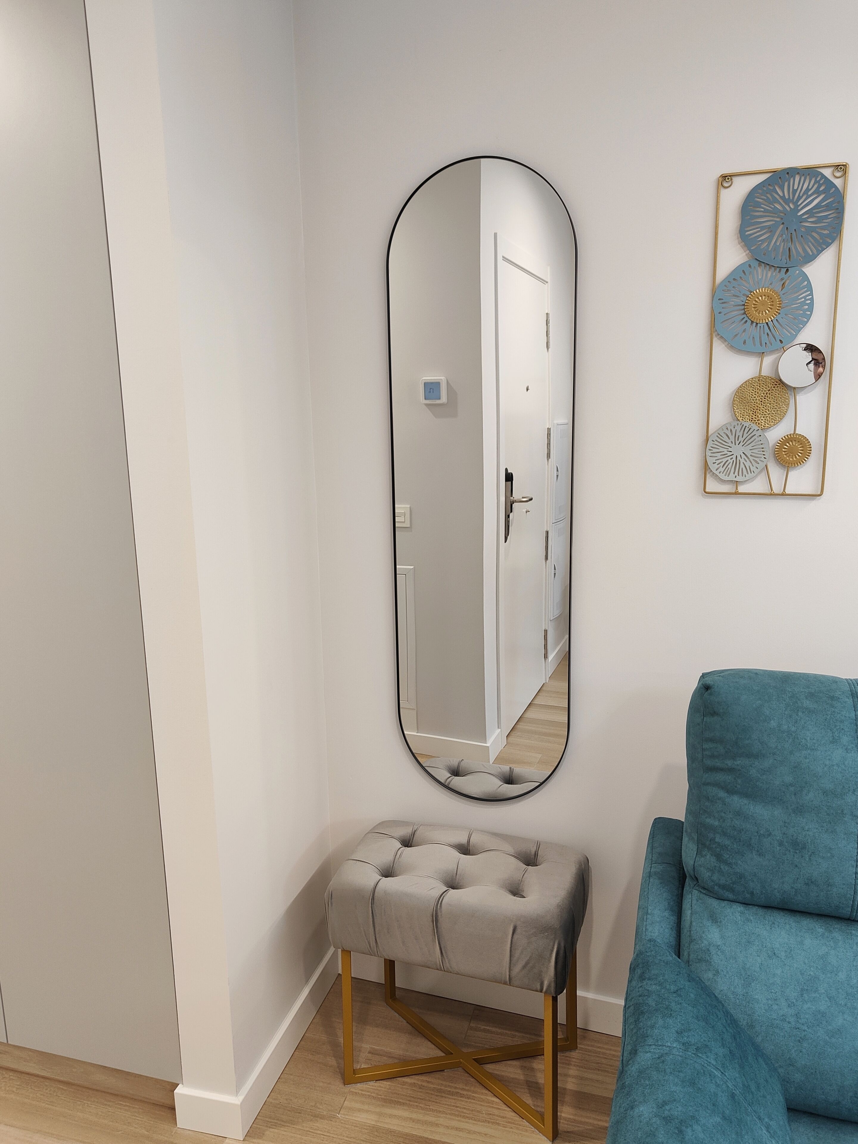 Una habitación con un espejo ovalado grande, un banco tapizado y un sillón color aguamarina.