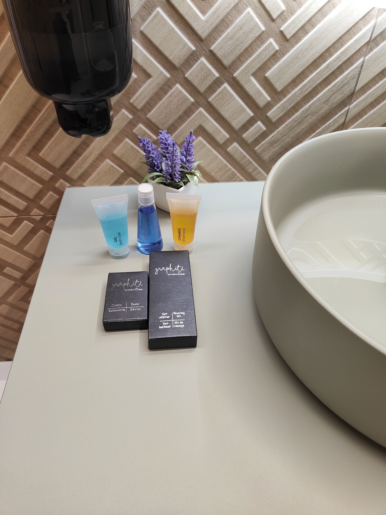 Een badkamer met een groot wastafel, een spiegel en toiletartikelen zoals zeep, shampoo en gel.