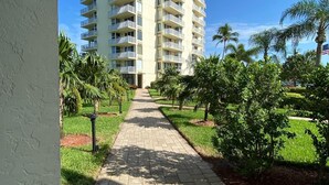 Uma trilha leva a um edifício alto com várias sacadas, cercado por vegetação e palmeiras.