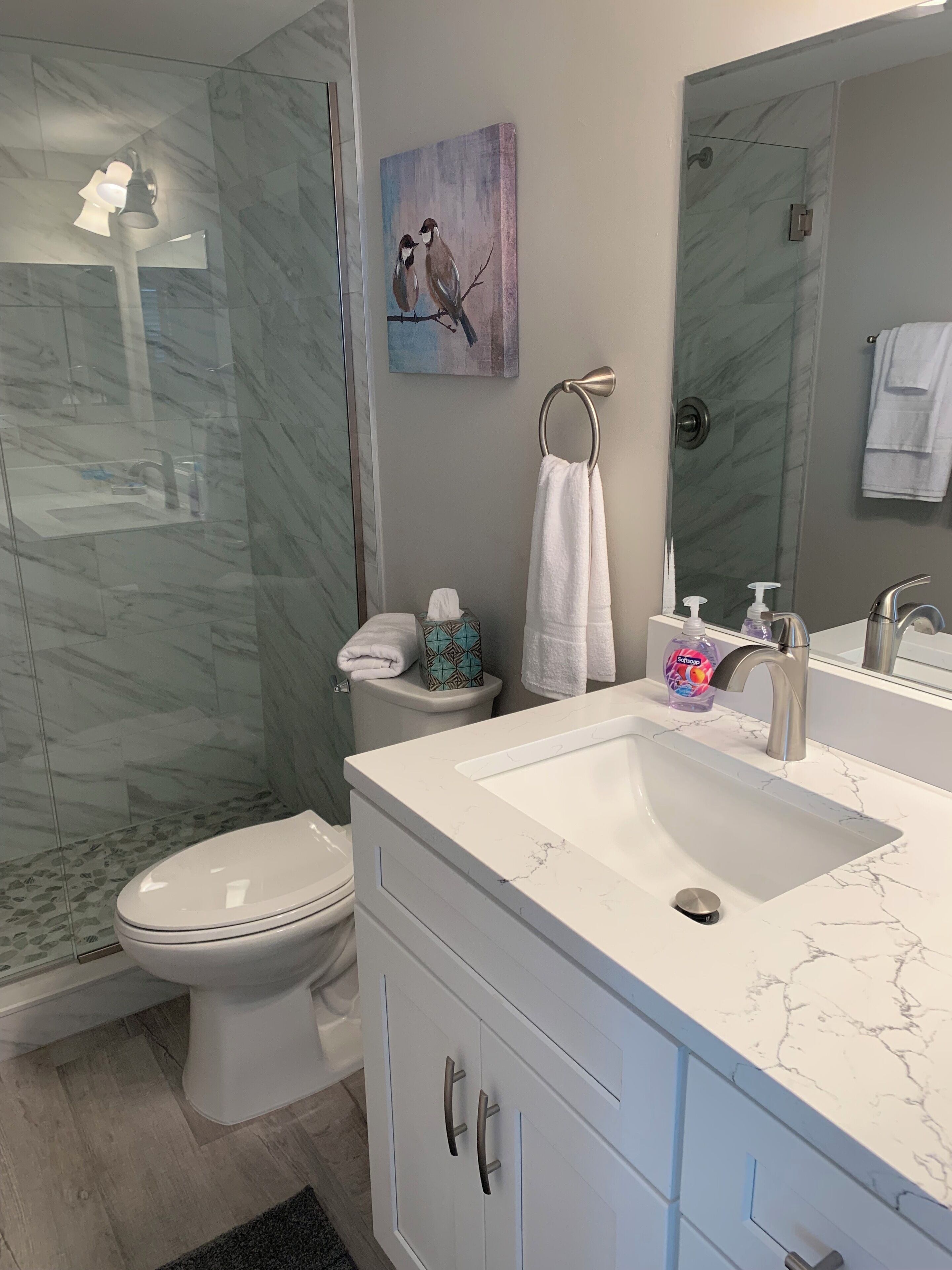 A modern bathroom with a marble sink, a glass shower enclosure, and a toilet.