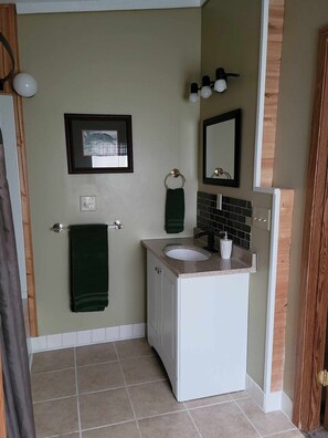 A bathroom with a white sink, a mirror, a framed picture on the wall, and a towel rack.