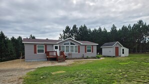 A single-story mobile home with a front porch, a garage, and a small attached shed.