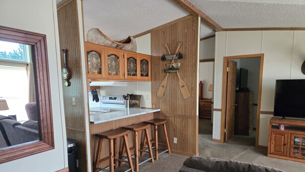 A compact living space with a kitchenette, wooden bar stools, a television, and a bookshelf.