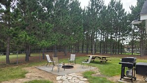 A backyard with a stone pathway, picnic table, chairs, and a grill.
