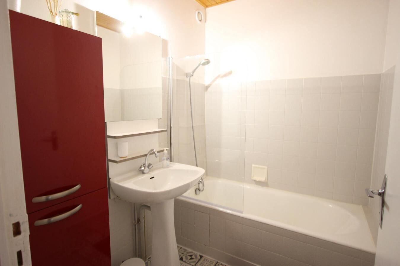 Un baño con lavamanos blanco, un espejo, ducha y armario rojo.