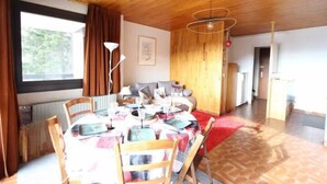 Een eetruimte met een houten plafond, een tafel gedekt voor vier personen, en uitzicht op een bos door een raam.