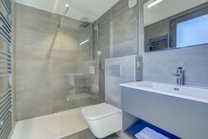 A modern bathroom with a glass-enclosed shower, a white toilet, and a large sink with a mirror above it.