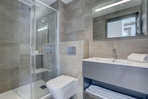 A modern bathroom with a glass shower enclosure, a toilet, a sink with a mirror, and a towel rack.