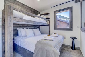 A bunk bed with white bedding and towels, a small round table, and a window with a view of a building and hills.