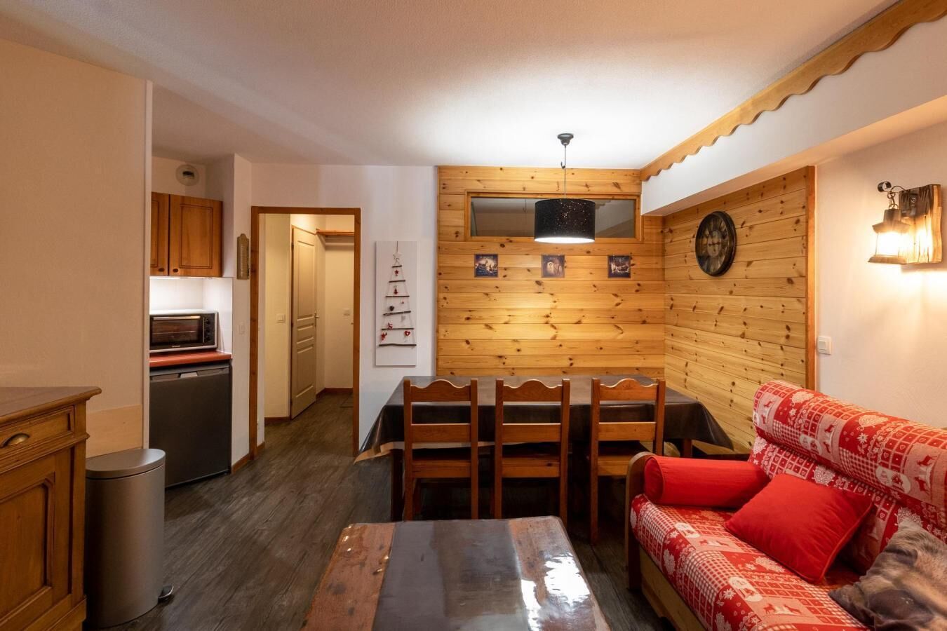 Un espacio habitable compacto con kitchenette, zona de comedor y sofá con cojines rojos.