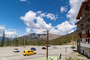 A parking lot with several cars, a yellow van, and a building with balconies. - Ground floor, fitness, swimming pool, sauna, balcony, tv, ski locker, 46m², Les Orres (Les Orres)