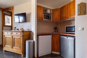 A compact kitchen with wooden cabinets, a microwave, a dishwasher, and a TV mounted on the wall. - Ground floor, fitness, swimming pool, sauna, balcony, tv, ski locker, 46m², Les Orres (Les Orres)