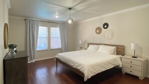 A bedroom with a large bed, a nightstand, a dresser, and a ceiling fan.