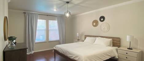 A bedroom with a large bed, a nightstand, a dresser, and a ceiling fan.