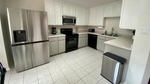A modern kitchen with white cabinets, stainless steel appliances, and a tiled floor.