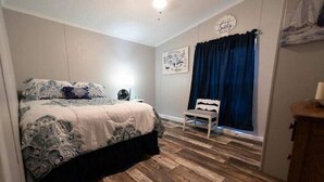 A bedroom with a bed, a bedside table, a chair, a window with curtains, and a wall with a sign.