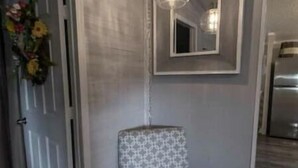 A corner of a room with a patterned chair, a hanging light fixture, and a mirror on the wall.