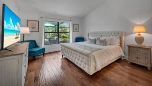 A bedroom with a large bed, a window with a view, a blue chair, and a wooden floor.