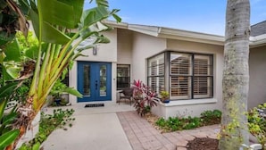 A two-story house with a blue door, large windows, and a small patio area with plants.
