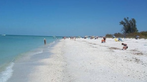 A beach with clear turquoise water, a sandy shore, and a few people and umbrellas.
