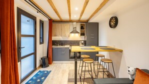 Una cocina compacta con techo de madera, un comedor con taburetes y una pequeña zona de estar con cojín.