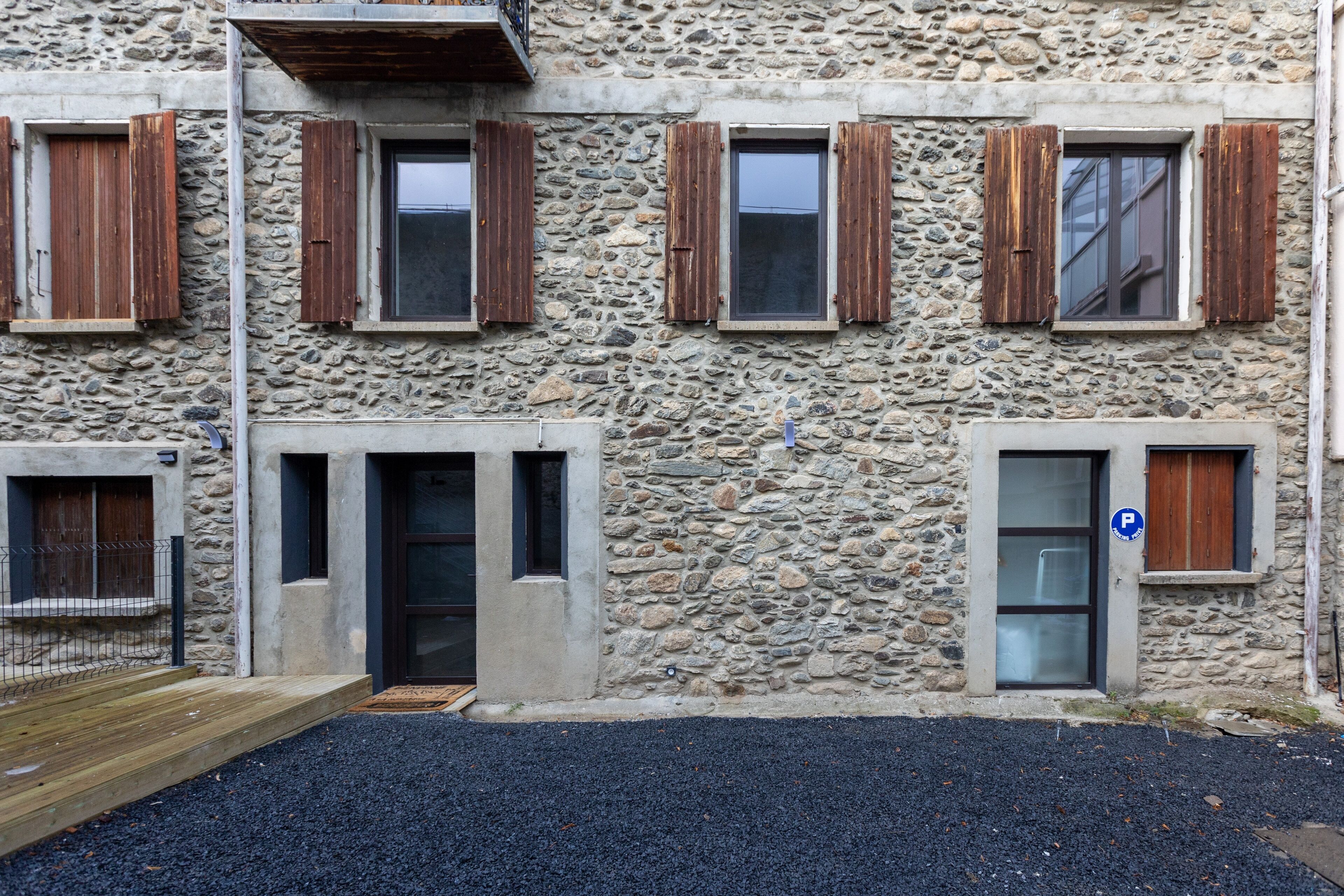 A stone building with multiple windows, some with wooden shutters, and a small parking sign.