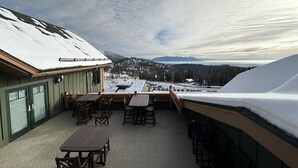 A covered outdoor patio with tables and chairs, a view of snow-covered mountains, and a building with green siding.