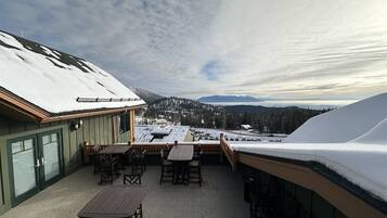 A covered outdoor patio with tables and chairs, a view of snow-covered mountains, and a building with green siding.