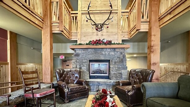 A lobby with a stone fireplace, leather chairs, a green sofa, and a deer antler decoration.