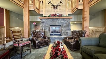 A lobby with a stone fireplace, leather chairs, a green sofa, and a deer antler decoration.