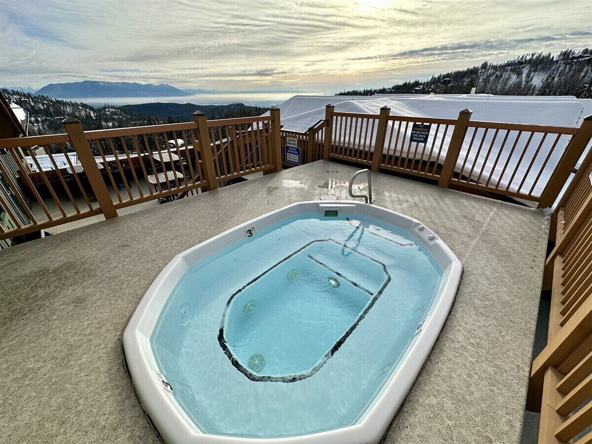 A hot tub on a deck with a view of mountains and a lake.