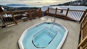 A hot tub on a deck with a view of mountains and a lake.