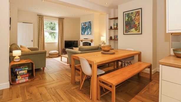 A modern living room with a wooden dining table, benches, and a TV in the background.