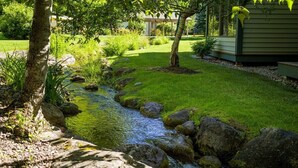 Un jardín tranquilo con un arroyo pequeño, rocas y abundante vegetación.