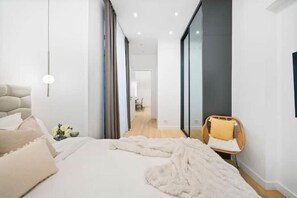 Een moderne slaapkamer met een groot bed, een nachtkastje met een lamp en een stoel.